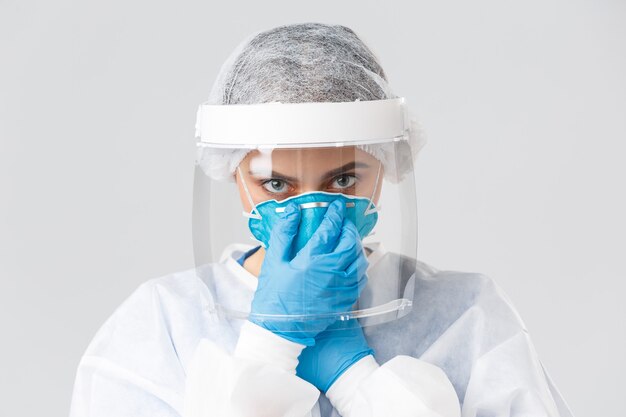 Covid-19, preventing virus, health, healthcare workers and quarantine concept. Close-up serious female doctor, nurse in personal protective equipment, put on respirator, look camera determined