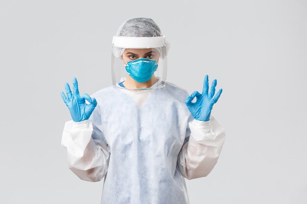 Covid-19, preventing virus, health, healthcare workers and quarantine concept. Confident doctor or nurse in protective equipment PPE, respirator, medical gloves show okay gesture