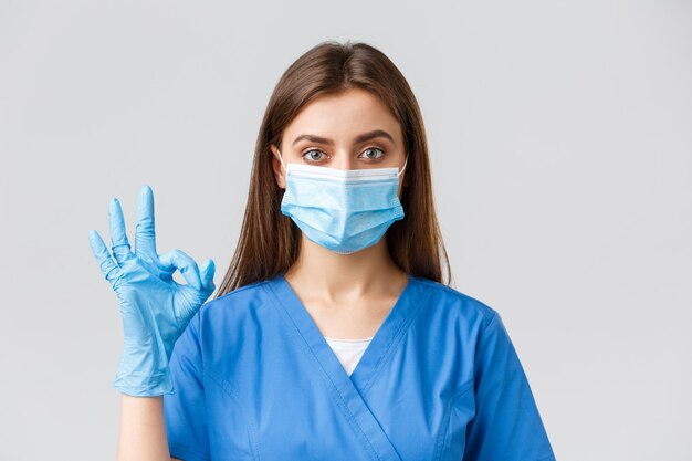 Covid-19、ウイルス、健康、医療従事者、検疫の概念を防ぎます。コロナウイルス患者と一緒に診療所で働いている自信のある女性看護師または医師が、医療用マスクを着用して、大丈夫な兆候を示しています