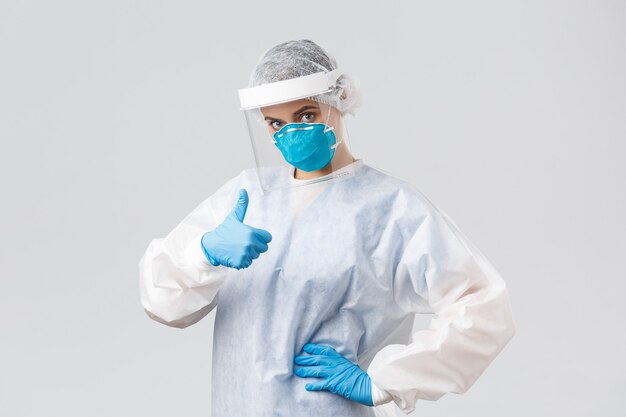 Covid-19, preventing virus, health, healthcare workers and quarantine concept. Confident serious doctor in personal protective equipment, female nurse show thumb-up, fighting coronavirus