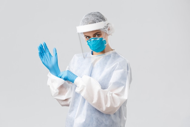 Covid-19, preventing virus, health, healthcare workers and quarantine concept. Determined young woman doctor, nurse in PPE protective equipment, face mask put on rubber gloves, working on vaccine