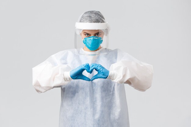 Covid-19, preventing virus, health, healthcare workers and quarantine concept. Doctor saving life patient from coronavirus pandemic, show heart sign, wear personal protective equipment, PPE costume