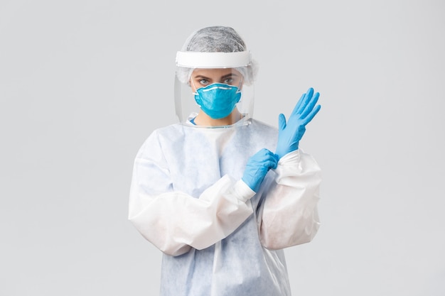 Covid-19, preventing virus, health, healthcare workers and quarantine concept. Serious female doctor in personal protective equipment PPE, shield, face mask out on gloves to enter patient room