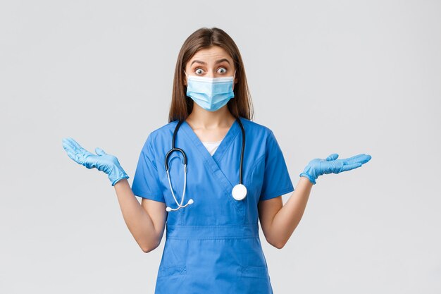 Covid-19、ウイルス、健康、医療従事者、検疫の概念を防ぎます。青いスクラブと医療用マスクを身に着けた驚きと興奮の女性看護師または医師は、手を横に広げて面白がっています