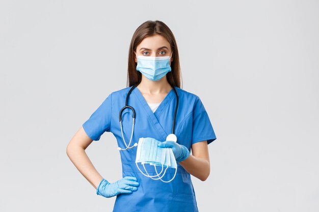 Covid-19, 바이러스, 건강, 의료 종사자 및 검역 개념을 예방합니다. 파란색 수술복을 입은 젊은 의사 또는 여성 간호사와 코로나바이러스 감염에 대한 보호 장비, 의료용 마스크 제공
