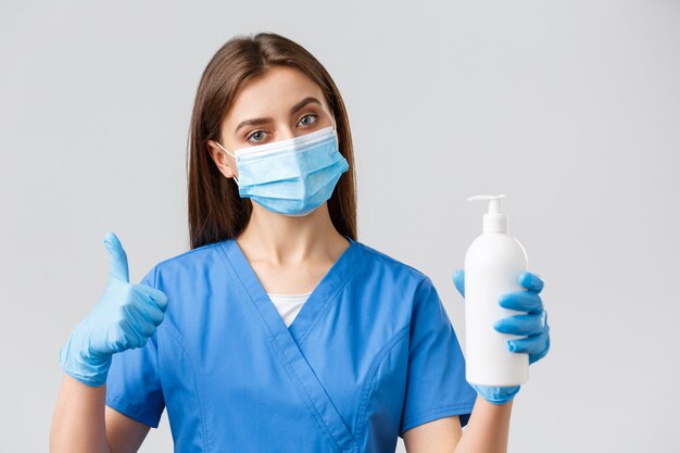 Covid-19, профилактика вируса, концепция медицинских работников. Серьезная медсестра или врач в синих скрабах, медицинской маске и перчатках рекомендуют использовать мыло или дезинфицирующее средство против коронавирусной инфекции.