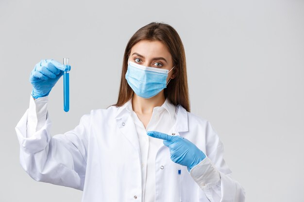 Covid-19, preventing virus, healthcare workers and quarantine concept. Doctor in personal protective equipment, medical mask and scrubs, pointing finger at test-tube coronavirus vaccine