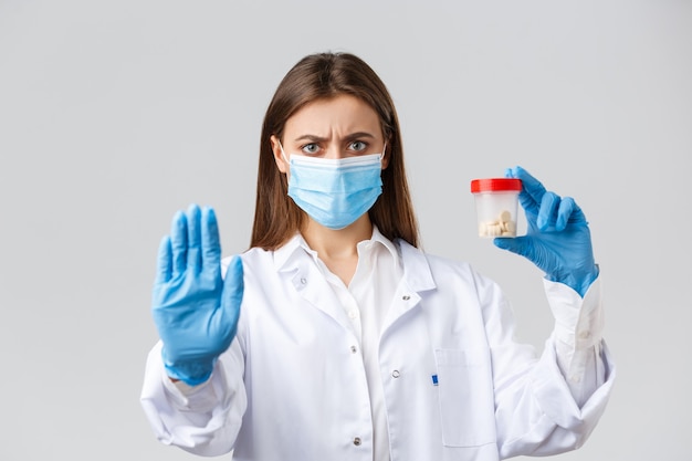 Covid-19, 바이러스, 의료 종사자 및 검역 개념을 예방합니다. 의료용 마스크와 PPE를 착용한 진지한 의사는 이 약의 사용을 중단하고 나쁜 약이나 항생제를 보여줍니다.