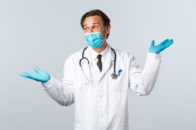 Covid-19, preventing virus, healthcare workers and vaccination concept. Charismatic doctor in medical mask and gloves, pointing sideways, showing two products, looking left intrigued