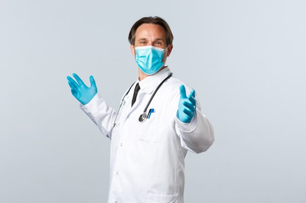 Covid-19, 바이러스, 의료 종사자 및 예방 접종 개념을 예방합니다. 의료용 마스크와 장갑을 끼고 기뻐하는 의사는 손을 옆으로 벌리고, 좋은 소식을 축하하고, 흰색 배경