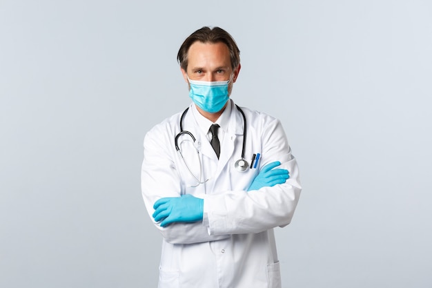 Free photo covid-19, preventing virus, healthcare workers and vaccination concept. confident and determined professional doctor in medical mask and gloves, cross arms chest, treating sick patients