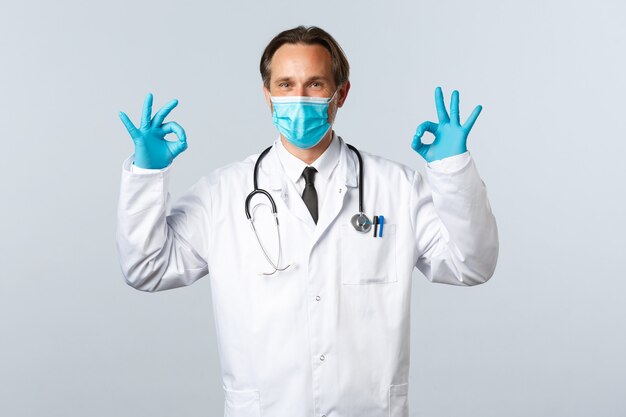Covid-19, 바이러스, 의료 종사자 및 예방 접종 개념을 예방합니다. 의사는 클리닉 서비스의 안전 또는 품질을 보장하고 승인 시 괜찮은 제스처를 보여주고 의료 마스크와 장갑을 착용합니다.
