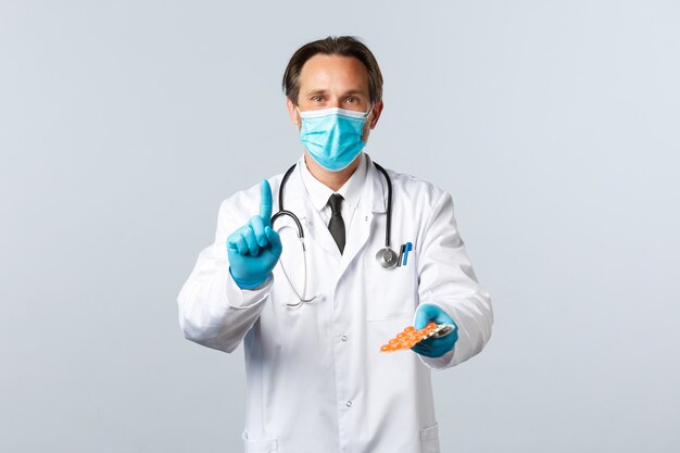 Covid-19、ウイルス、医療従事者、予防接種の概念を防ぎます。医療用マスクと手袋をはめた医師が処方箋を説明し、薬を与え、1本の指を見せて患者に錠剤を渡します