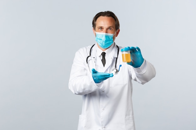Covid-19、ウイルス、医療従事者、予防接種の概念を防ぎます。満足のいく表情、白い背景で尿サンプルを示す医療マスクと手袋で興奮したラボクリニックの医師