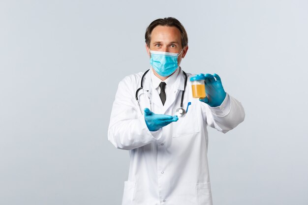 Covid-19, 바이러스, 의료 종사자 및 예방 접종 개념을 예방합니다. 의료 마스크와 장갑을 끼고 만족스러운 표정으로 소변 샘플을 보여주는 흥분한 실험실 클리닉 의사, 흰색 배경