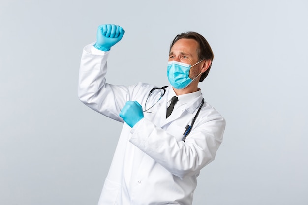 Covid-19, preventing virus, healthcare workers and vaccination concept. Happy triumphing doctor in medical mask and gloves celebrating good news, fist pump and dancing, white background