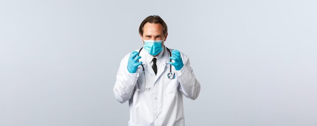 Covid-19, профилактика вируса, медицинские работники и концепция вакцинации. Безумно раздраженный доктор устал от людей, не соблюдающих правила социального дистанцирования, сердито сжимает кулаки, носит маску и перчатки