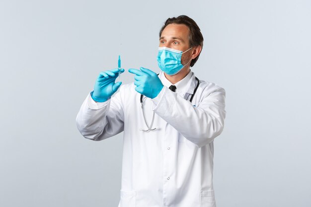 Covid-19, preventing virus, healthcare workers and vaccination concept. Middle-aged doctor in medical mask and gloves holding syringe with coronavirus vaccine or hiv prep, prepare shot for patient