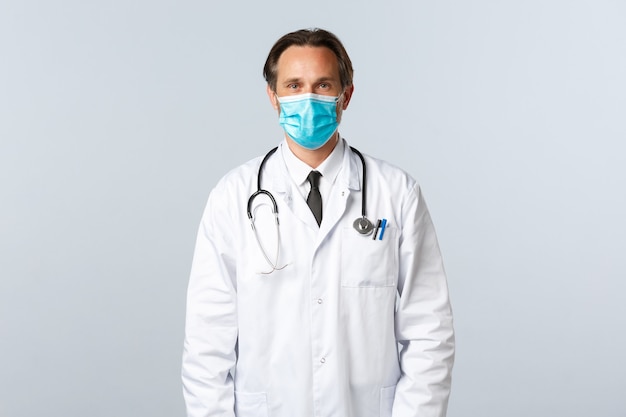 Covid-19、ウイルス、医療従事者、予防接種の概念を防ぎます。白衣と医療マスクを身に着けた中年のプロのセラピストがクリニックで患者の話を聞き、医師が仕事をしている
