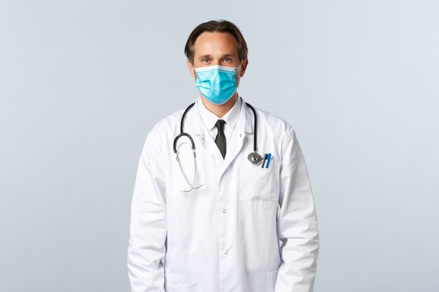 Covid-19, 바이러스, 의료 종사자 및 예방 접종 개념을 예방합니다. 흰색 코트와 의료 마스크를 쓴 중년 전문 치료사는 병원에서 환자의 말을 듣고 직장에서 의사