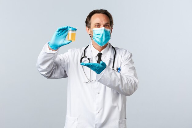 Covid-19, 바이러스, 의료 종사자 및 예방 접종 개념을 예방합니다. 의료용 마스크와 장갑을 끼고 웃는 의사는 깨끗한 테스트 결과에 만족하고 흰색 배경에 소변 샘플을 보여줍니다.