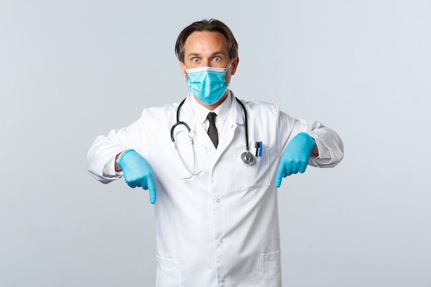 Covid-19, профилактика вируса, медицинские работники и концепция вакцинации. Шокированный задыхающийся мужчина-врач в медицинской маске и гвоздики реагирует на процент вспышки коронавируса, указывая пальцами вниз