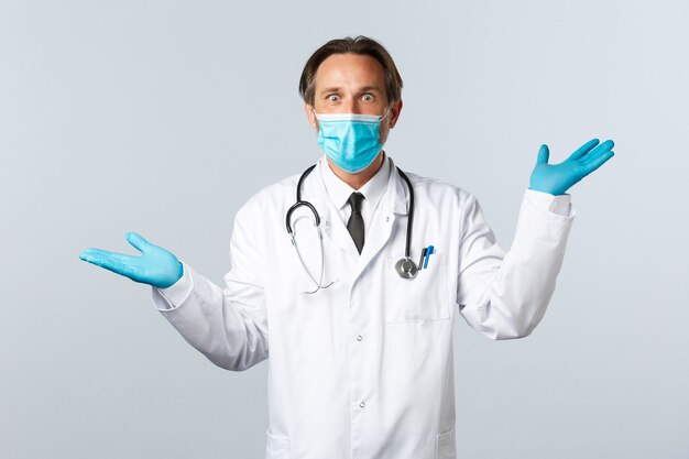 Covid-19, 바이러스, 의료 종사자 및 예방 접종 개념을 예방합니다. 충격을 받은 남성 의사는 의료용 마스크와 장갑을 끼고 손을 들고 좌우 두 개의 제품을 보여줍니다.