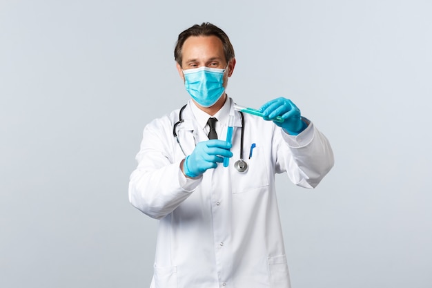 Covid-19、ウイルス、医療従事者、予防接種の概念を防ぎます。別の試験管に化学成分を注いで、ワクチンテストを実施する医療マスクと手袋で笑顔の医師