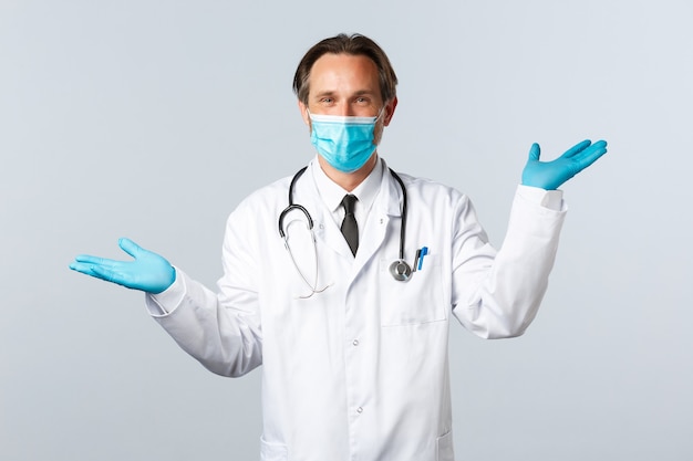 Covid-19, preventing virus, healthcare workers and vaccination concept. Smiling handsome doctor give two variants, wear medical mask and gloves, showing left and right products, white background