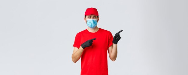 Covid-19, self-quarantine, online shopping and shipping concept. Upset and displeased delivery guy staring and pointing right with reluctant bothered face, wear uniform, medical mask and gloves