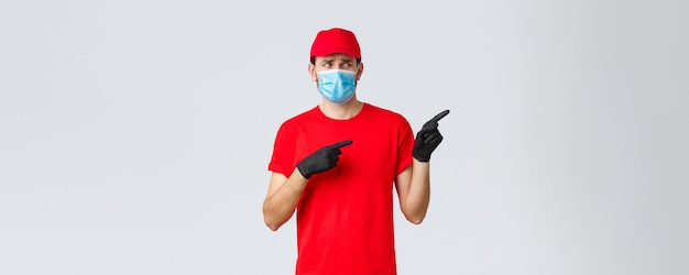 Covid-19, self-quarantine, online shopping and shipping concept. Upset and displeased delivery guy staring and pointing right with reluctant bothered face, wear uniform, medical mask and gloves