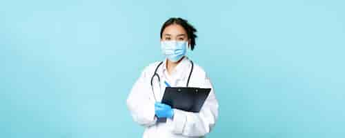 無料写真 クリップボードshiを保持しているフェイスマスクでアジアの女性医師の看護師を笑顔のcovidと検疫の概念