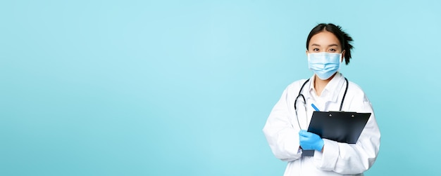 Бесплатное фото Концепция covid и карантина улыбающаяся азиатская женщина-врач-медсестра в маске для лица с буфером обмена ши