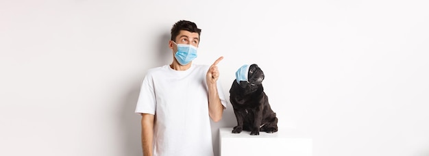 Free photo covid animals and quarantine concept young man and black dog wearing medical masks pug and owner loo