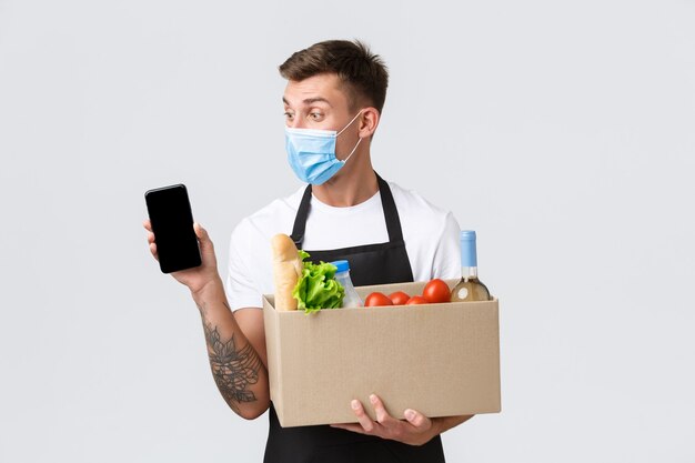 医療マスクのCovid非接触ショッピングと食料品配達のコンセプトハンサムなセールスマンは提案します...