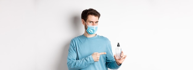 Free photo covid health and quarantine concept caucasian man in medical mask pointing finger at bottle with han