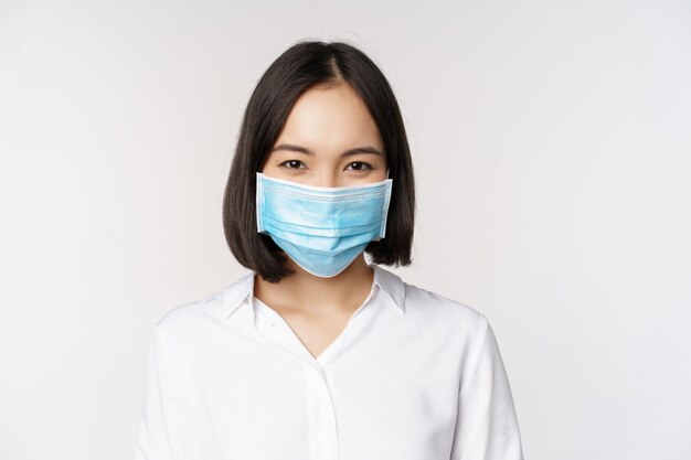 코비드 및 의료 개념 대유행 흰색 배경 동안 코로나바이러스로부터 보호를 사용하여 웃는 얼굴 마스크에 아시아 여성 사무실 여성의 초상화를 닫습니다