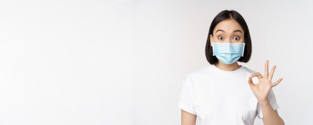 Covidヘルスケアと医療の概念は、驚いて見せびらかしているように見える医療マスクのアジアの女性に感銘を与えました