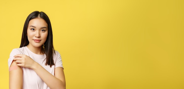 Foto gratuita covid e il concetto medico sanitario sorridente ragazza coreana mostra la spalla con la toppa ha preso il colpo di coro