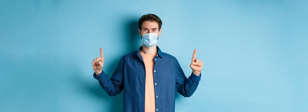 Free photo covid and lifestyle concept handsome young man in face mask looking healthy and happy pointing finge