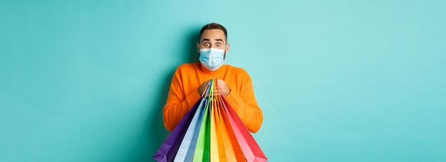 Free photo covid pandemic and lifestyle concept excited man in face mask showing shopping bags and rejoicing fr