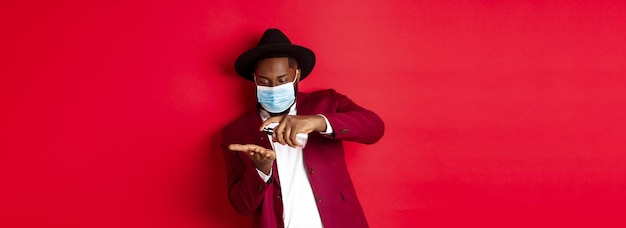 Covid quarantine and holidays concept handsome black man in face mask and party outfit disinfecting