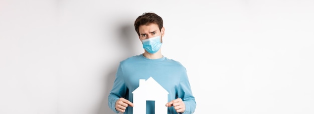 Free photo covid and real estate concept sad and doubtful young man in medical mask feeling reluctant showing p