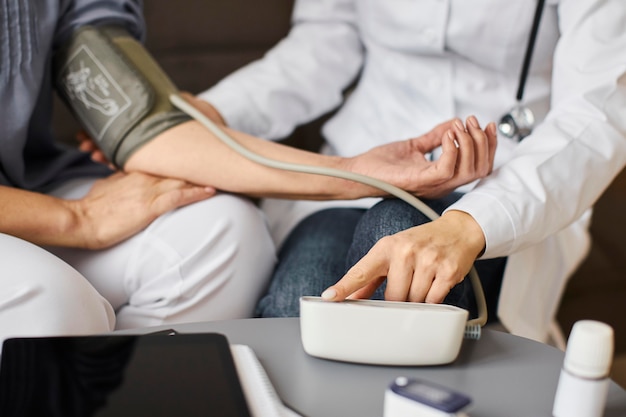 Free photo covid recovery center female doctor checking elder patient's blood pressure with aparatus