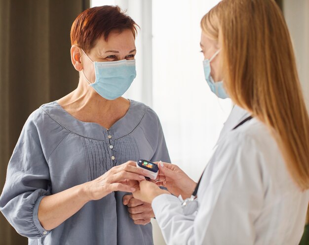 Covid recovery center female doctor with medical mask checking elder patient's oxygen level