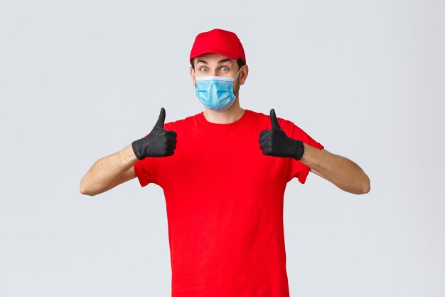 Covid selfquarantine shopping and shipping concept enthusiastic and happy courier in red uniform glo...