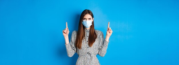 Free photo covid social distancing and healthcare concept angry woman frowning in medical mask pointing and loo