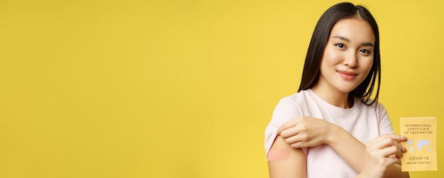 Free photo covid and tourism concept portrait of young asian woman showing her patch from covid vaccine holding