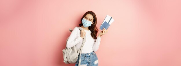 Covid and travelling concept happy woman traveller in medical mask holding passport and airplane tic