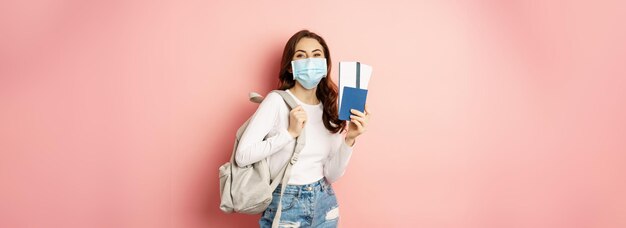 Covid and travelling concept happy woman traveller in medical mask holding passport and airplane tic